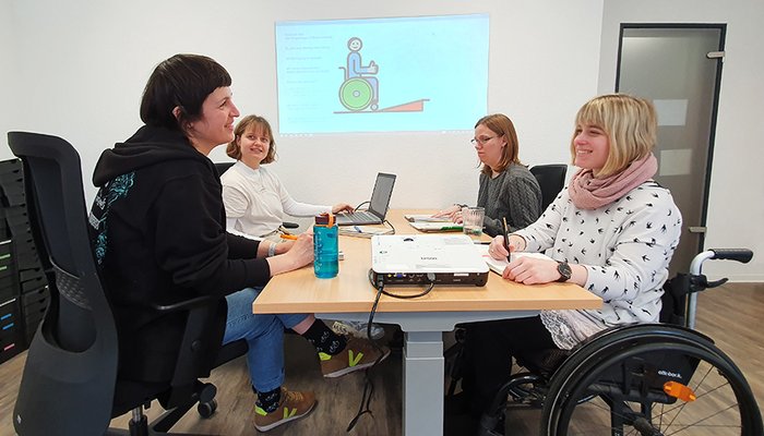 4 Frauen mit und ohne Behinderung sitzen an einem Besprechungstisch