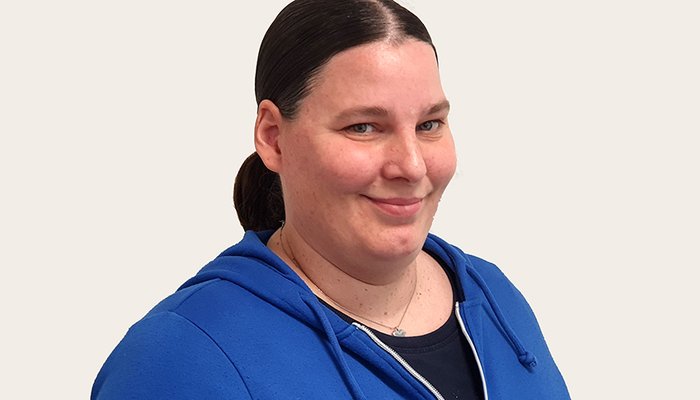  Frau mit dunklen Haaren, Zopf und blauer Jacke lächelt in die Kamera