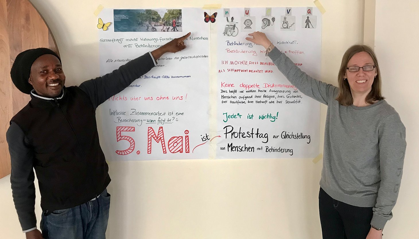 Ein Mitarbeiter und eine Mitarbeiterin zeigen auf ein Plakat mit Schrift.