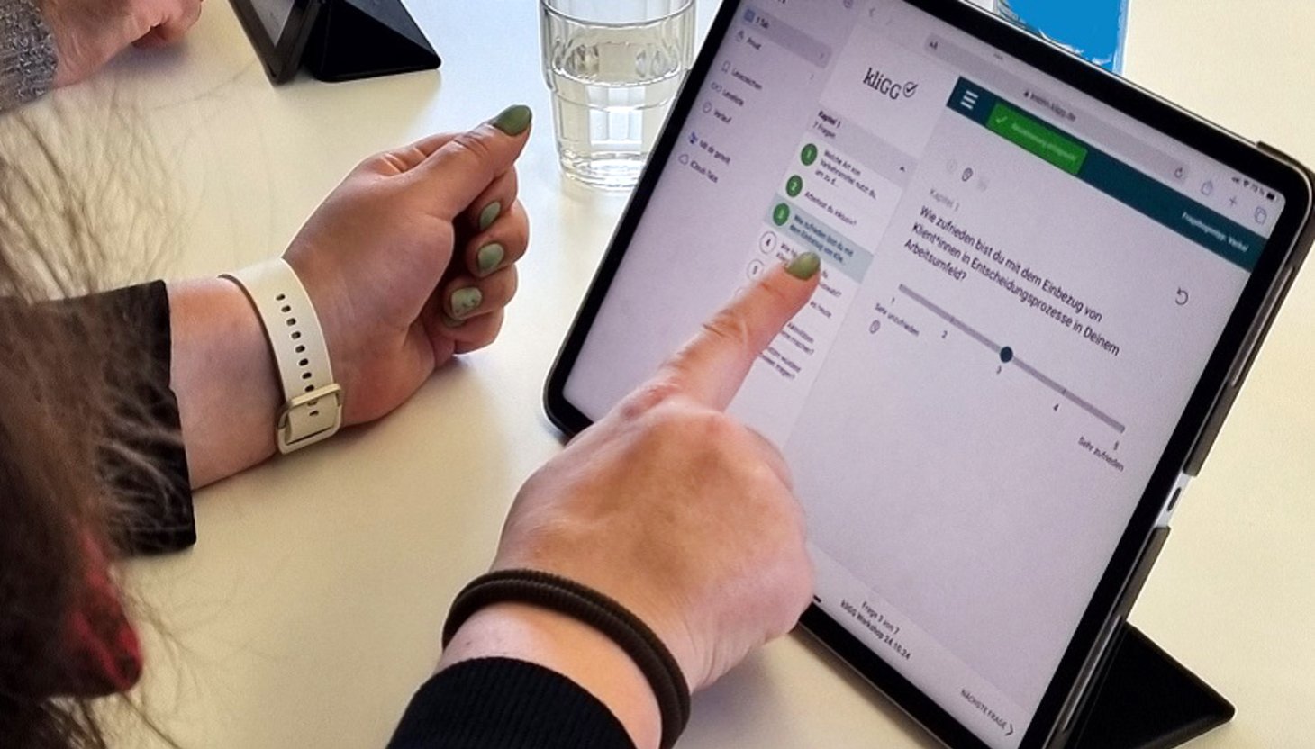Es ist ein Tablet zu sehen und die Hände einer Frau, die das Tablet bedient.