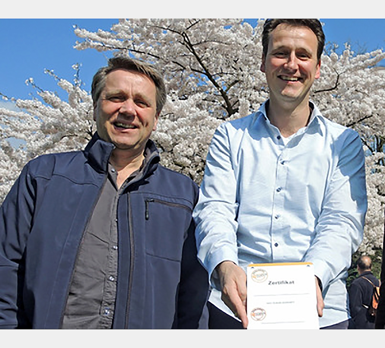 Ein Mitarbeiter von alsterdorf assistenz west zeigt lächelnd das erste nueva-Zertifikat in Hamburg.